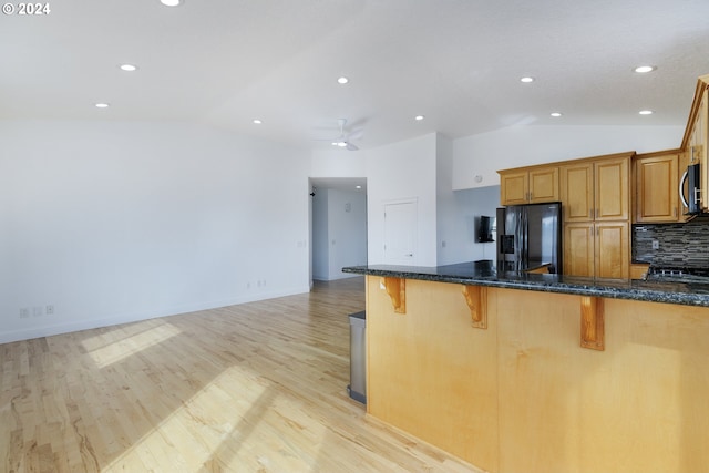 kitchen with decorative backsplash, black refrigerator with ice dispenser, a breakfast bar, dark stone countertops, and light hardwood / wood-style floors