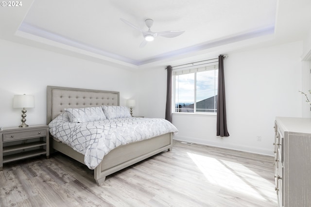 bedroom featuring a raised ceiling, ceiling fan, and light wood-type flooring