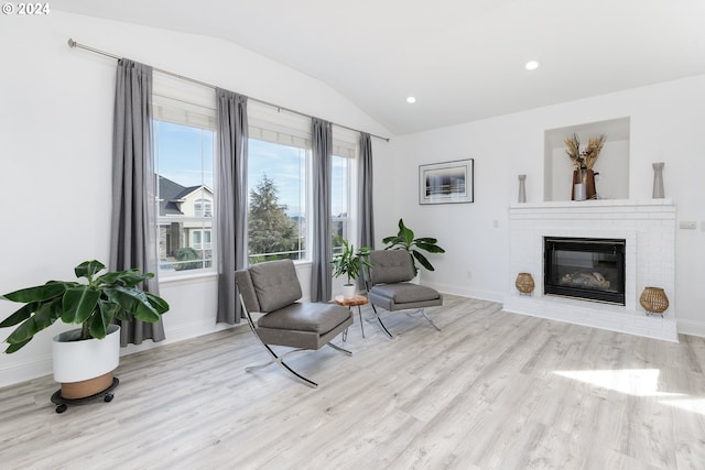 sitting room featuring a brick fireplace, vaulted ceiling, and light wood-type flooring