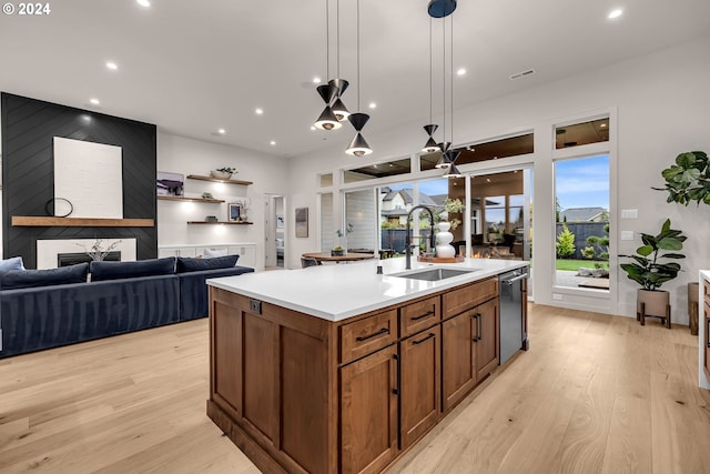 kitchen featuring a kitchen island with sink, sink, decorative light fixtures, a fireplace, and light hardwood / wood-style floors