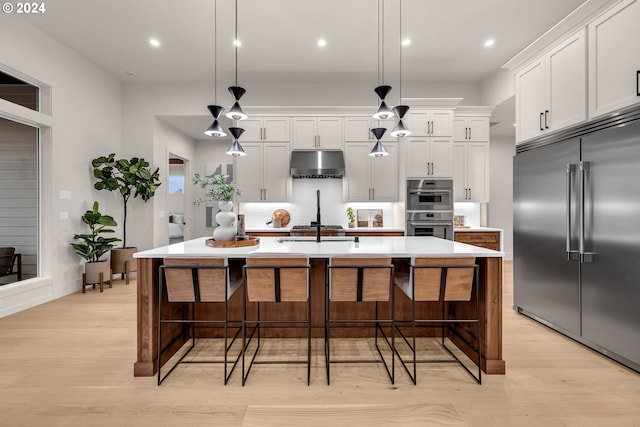 kitchen featuring a kitchen island with sink, pendant lighting, stainless steel appliances, and light hardwood / wood-style floors