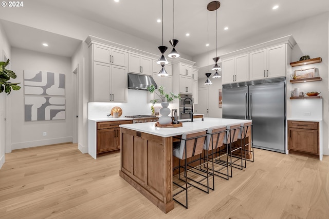 kitchen featuring white cabinets, a center island with sink, and built in fridge