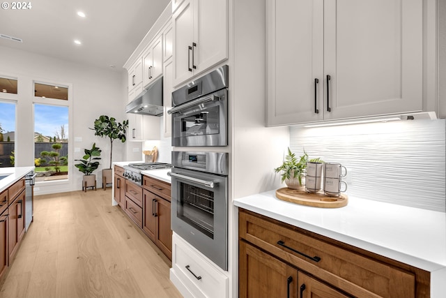 kitchen with stainless steel appliances, white cabinetry, tasteful backsplash, and light hardwood / wood-style flooring