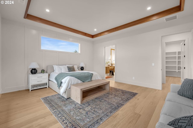 bedroom featuring a tray ceiling, a spacious closet, ensuite bathroom, and light wood-type flooring