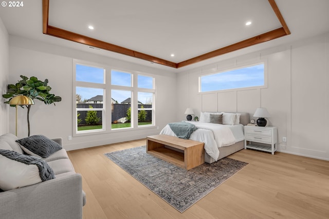 bedroom with a raised ceiling, light wood-type flooring, and multiple windows