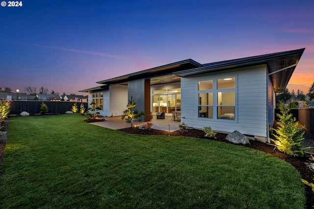 back house at dusk with a patio area and a yard