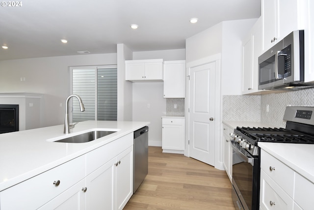 kitchen featuring appliances with stainless steel finishes, sink, backsplash, white cabinetry, and light hardwood / wood-style flooring