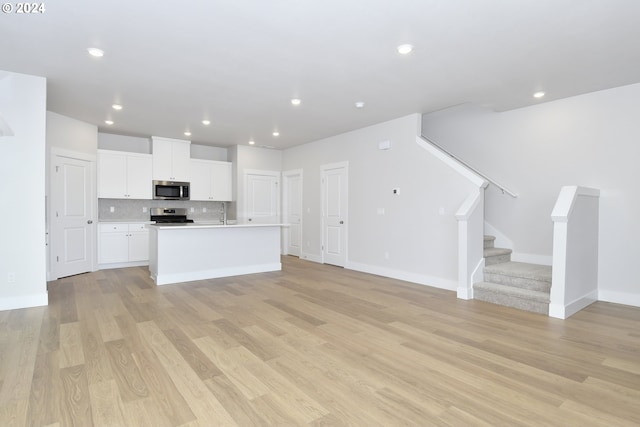 kitchen featuring decorative backsplash, a center island with sink, white cabinetry, appliances with stainless steel finishes, and light hardwood / wood-style floors