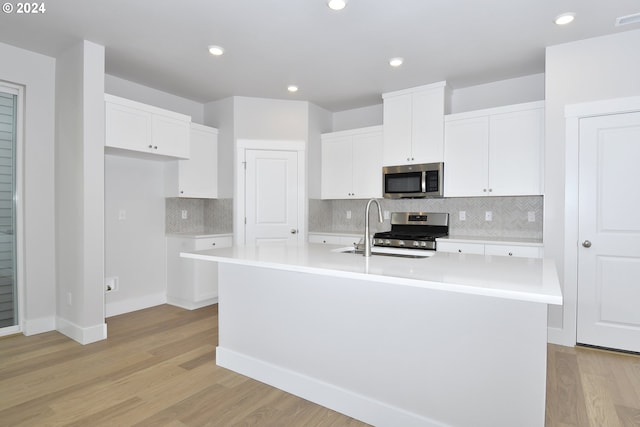 kitchen with appliances with stainless steel finishes, sink, a center island with sink, and light wood-type flooring