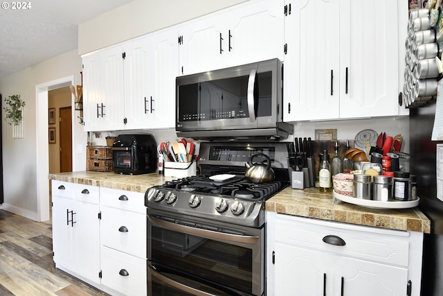 kitchen with stainless steel appliances, a textured ceiling, light hardwood / wood-style flooring, and white cabinets