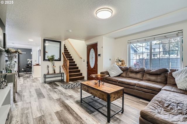 living room with a textured ceiling, stairway, and light wood-style floors