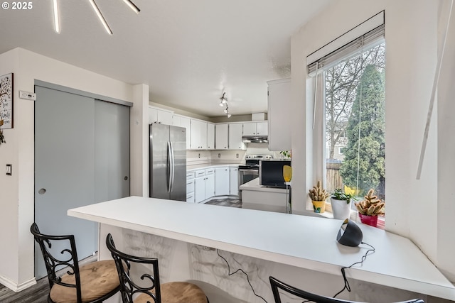 kitchen featuring white cabinets, a breakfast bar, a peninsula, stainless steel appliances, and under cabinet range hood