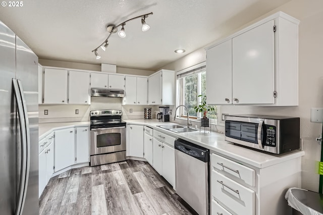 kitchen featuring stainless steel appliances, light countertops, a sink, light wood-type flooring, and under cabinet range hood