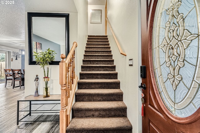 staircase with a textured ceiling and wood finished floors