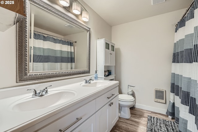 bathroom featuring heating unit, toilet, a sink, and wood finished floors