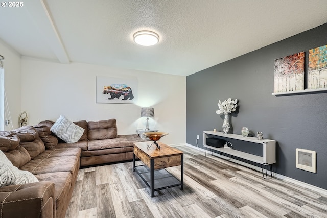 living area with a textured ceiling, heating unit, wood finished floors, and baseboards