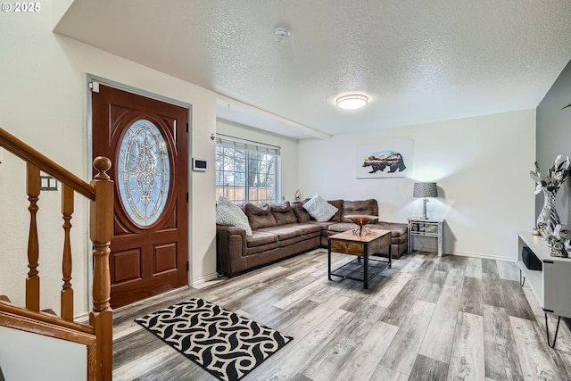 foyer entrance featuring a textured ceiling, stairway, light wood-type flooring, and baseboards