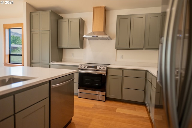 kitchen with appliances with stainless steel finishes, light hardwood / wood-style floors, gray cabinetry, and wall chimney range hood