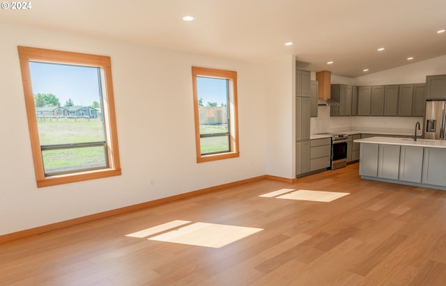 kitchen with a wealth of natural light, stainless steel appliances, vaulted ceiling, and light wood-type flooring