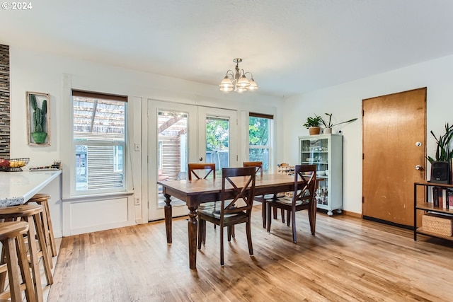 dining space featuring a healthy amount of sunlight, light wood-type flooring, and a notable chandelier