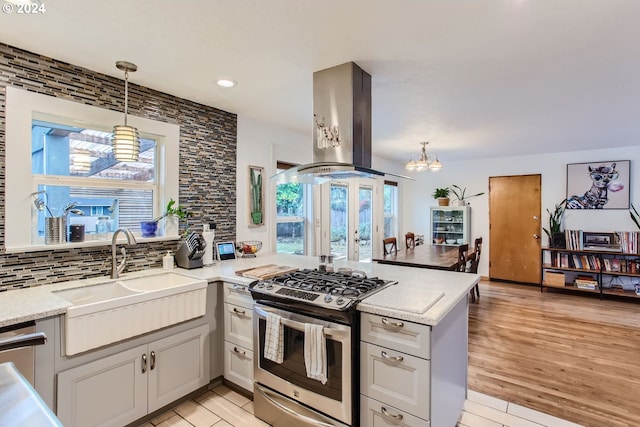 kitchen featuring island range hood, stainless steel gas range, hanging light fixtures, sink, and light hardwood / wood-style floors