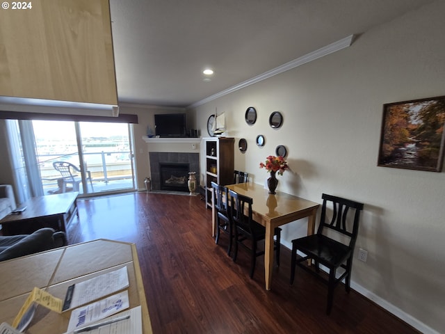 dining space featuring dark hardwood / wood-style floors, ornamental molding, and a tiled fireplace