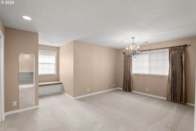 spare room with light colored carpet, a textured ceiling, and a notable chandelier