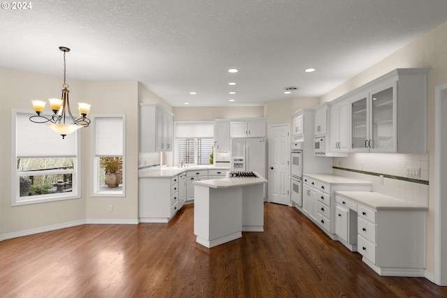 kitchen with white cabinets, dark hardwood / wood-style floors, a kitchen island, and white appliances