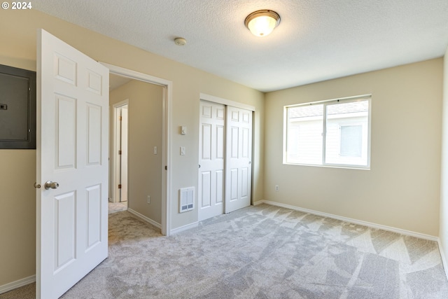 unfurnished bedroom featuring a textured ceiling, a closet, electric panel, and light colored carpet