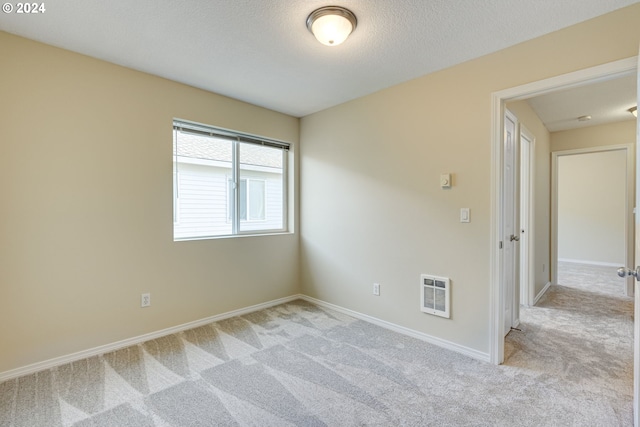 empty room featuring heating unit, light carpet, and a textured ceiling