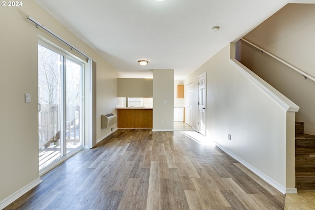 unfurnished living room with light wood-type flooring and an AC wall unit