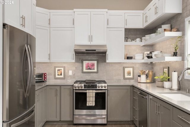 kitchen featuring tasteful backsplash, wall chimney range hood, gray cabinets, appliances with stainless steel finishes, and sink