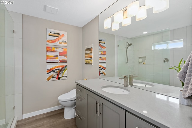 bathroom featuring a textured ceiling, toilet, vanity, wood-type flooring, and a tile shower