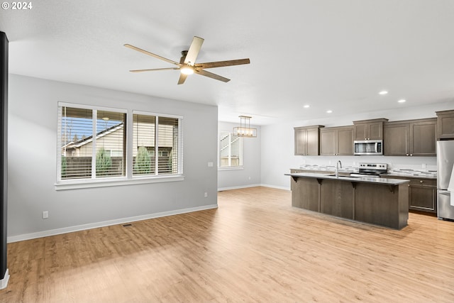 kitchen with a center island with sink, a kitchen breakfast bar, sink, appliances with stainless steel finishes, and light hardwood / wood-style floors