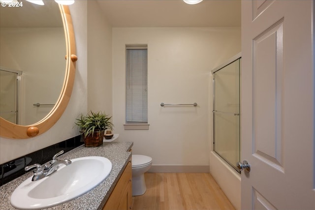 full bathroom with hardwood / wood-style floors, combined bath / shower with glass door, toilet, and vanity