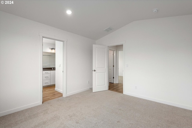 unfurnished bedroom featuring vaulted ceiling, ensuite bath, and light carpet