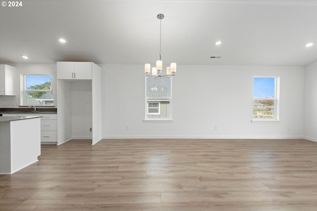 unfurnished living room featuring a notable chandelier, light wood-type flooring, a healthy amount of sunlight, and sink