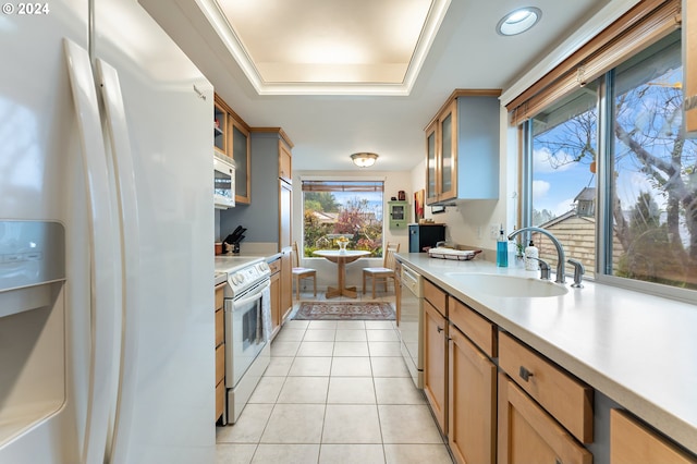 kitchen with light tile patterned floors, white appliances, a raised ceiling, and sink