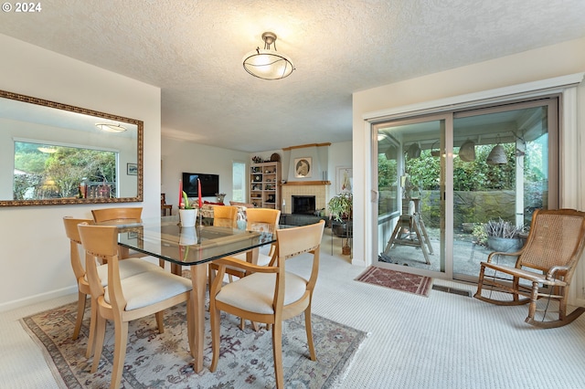 dining space featuring a tiled fireplace, carpet, and a textured ceiling