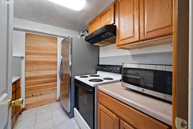 kitchen featuring electric range, light tile patterned flooring, and wood walls