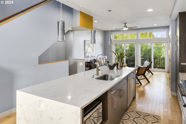 kitchen with a center island with sink, ceiling fan, pendant lighting, sink, and light hardwood / wood-style flooring