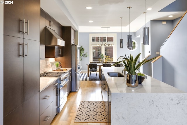 kitchen with extractor fan, light hardwood / wood-style flooring, decorative light fixtures, stainless steel appliances, and backsplash