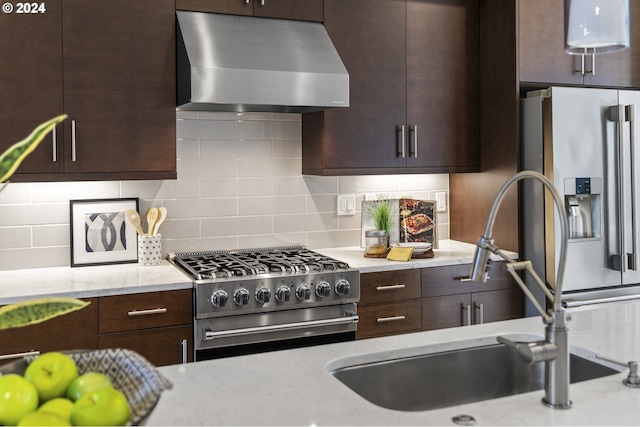 kitchen featuring light stone counters, stainless steel appliances, wall chimney range hood, decorative backsplash, and dark brown cabinetry