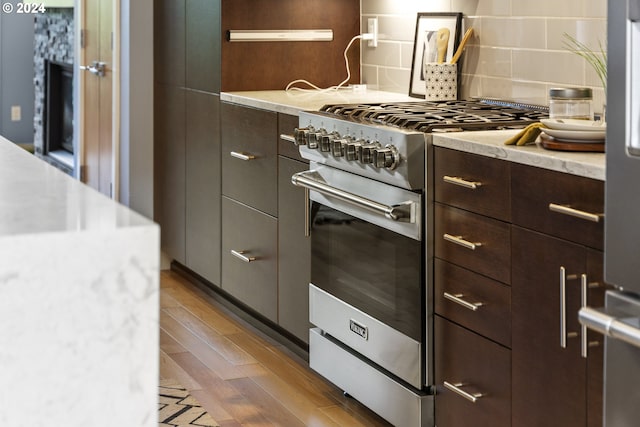 kitchen with dark brown cabinetry, stainless steel stove, tasteful backsplash, and light hardwood / wood-style flooring