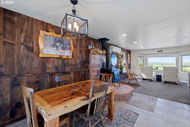 dining space featuring a wall unit AC, a wood stove, a notable chandelier, light carpet, and wooden walls