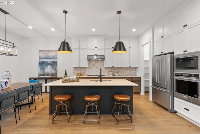 kitchen featuring a kitchen island with sink, hanging light fixtures, a breakfast bar, and appliances with stainless steel finishes