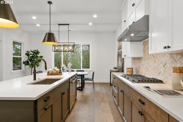 kitchen with sink, appliances with stainless steel finishes, hanging light fixtures, white cabinets, and a center island with sink