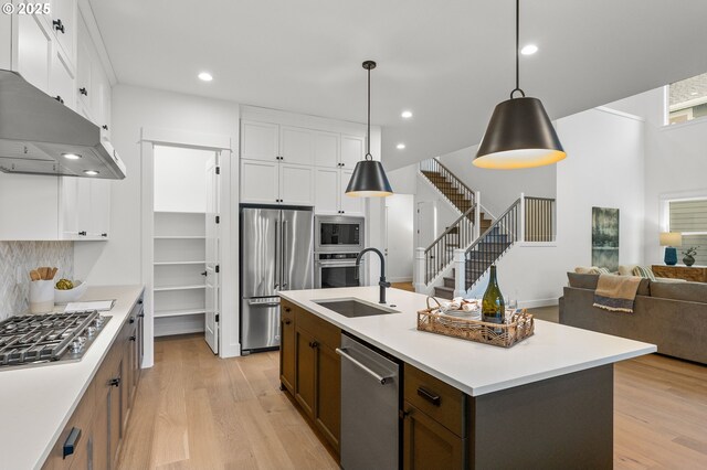 kitchen with sink, white cabinetry, decorative light fixtures, stainless steel appliances, and a kitchen island with sink