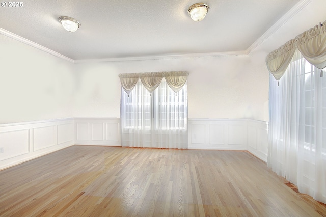 empty room with a textured ceiling, a healthy amount of sunlight, light wood-type flooring, and ornamental molding