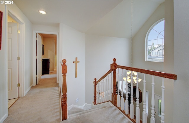 corridor with a notable chandelier, light colored carpet, and lofted ceiling